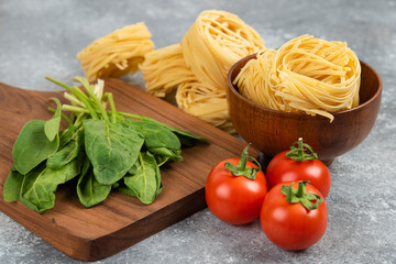 Wooden board with fresh vegetables and raw noodles on marble surface