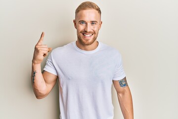 Young caucasian man wearing casual white tshirt smiling with an idea or question pointing finger up with happy face, number one