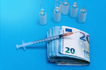 20 euro banknotes folded in a bundle and syringe resting on top next to doses of vials with white...