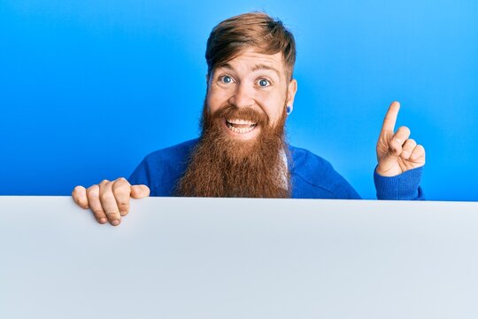 Young irish redhead man holding blank empty banner smiling happy pointing with hand and finger to the side