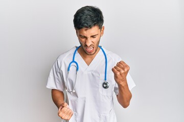 Young handsome man wearing doctor uniform and stethoscope celebrating surprised and amazed for success with arms raised and eyes closed