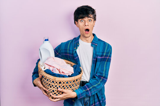 Handsome hipster young man holding laundry basket and detergent bottle afraid and shocked with surprise and amazed expression, fear and excited face.