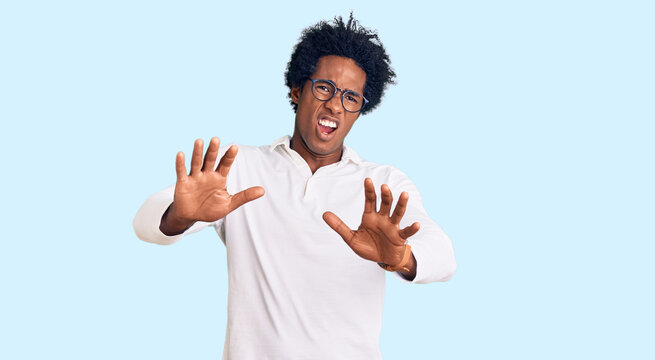 Handsome african american man with afro hair wearing casual clothes and glasses afraid and terrified with fear expression stop gesture with hands, shouting in shock. panic concept.