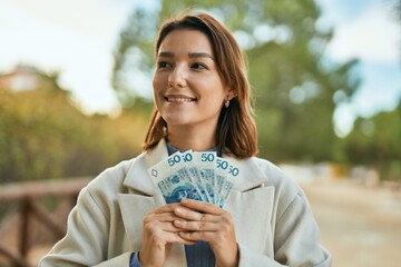 Young hispanic woman smiling happy holding polish zloty banknotes at the park