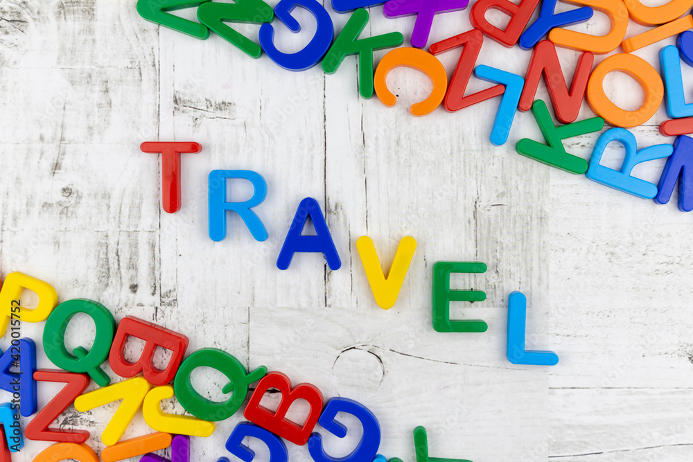 Fototapete word - travel - in bright colorful letters arranged diagonally on grey wood background with corner b