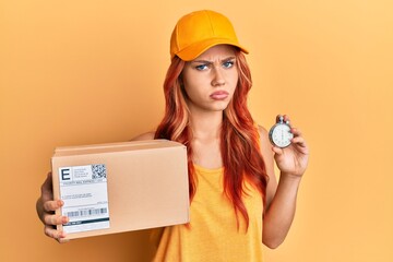 Young redhead woman holding delivery package and stopwatch skeptic and nervous, frowning upset because of problem. negative person.