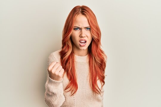 Young beautiful redhead woman wearing casual winter sweater angry and mad raising fist frustrated and furious while shouting with anger. rage and aggressive concept.