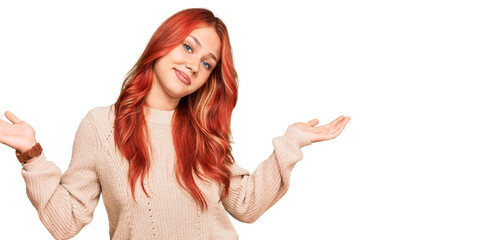 Young redhead woman wearing casual winter sweater clueless and confused expression with arms and...