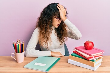 Young hispanic girl studying for school exam surprised with hand on head for mistake, remember error. forgot, bad memory concept.