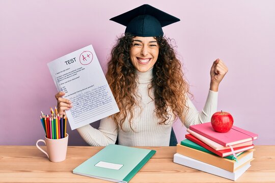 Young hispanic girl wearing graduated hat holding passed test screaming proud, celebrating victory and success very excited with raised arm