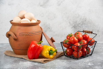 Pot of raw eggs, tomatoes and bell peppers on marble background