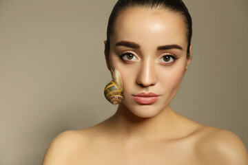 Beautiful young woman with snail on her face against beige background © New Africa