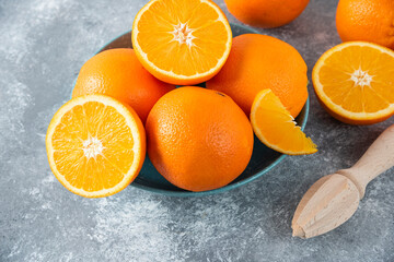 A bowl full of sliced and whole juicy orange fruits with wooden reamer