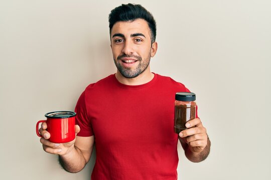 Young hispanic man holding cup of soluble coffee smiling with a happy and cool smile on face. showing teeth.