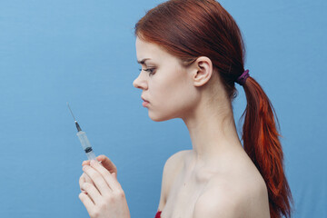 Obraz premium woman with syringe in hands on blue background injection rejuvenation botox side view