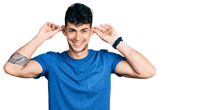 Young hispanic man wearing casual t shirt smiling pulling ears with fingers, funny gesture. audition problem