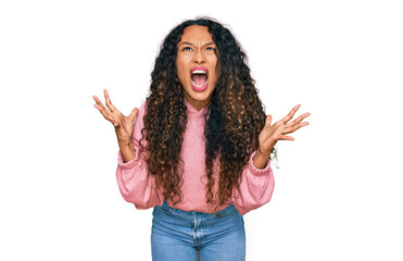 Young hispanic woman with curly hair wearing casual sweatshirt crazy and mad shouting and yelling with aggressive expression and arms raised. frustration concept.