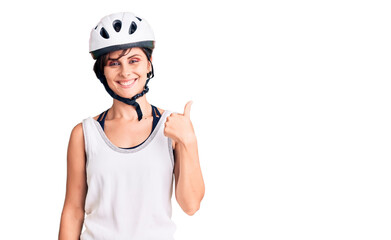 Beautiful young woman with short hair wearing bike helmet smiling happy and positive, thumb up doing excellent and approval sign