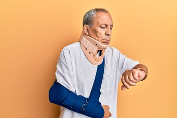 Handsome mature senior man wearing cervical collar and arm on sling checking the time on wrist watch, relaxed and confident