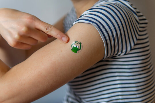 Woman pointing her arm with a fun, colorful, adhesive bandage after injection of vaccine or a scratch on the skin. First aid. Medical, pharmacy, and healthcare concept. After vaccination treatment.