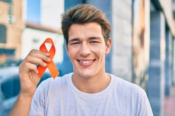 Young caucasian man smiling happy holding orange ribbon at the city.