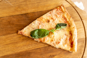 Slice of Pizza Margherita with mozzarella and basil leaves on wooden stend. Traditional italian food
