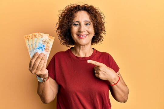 Beautiful middle age mature woman holding 10 swiss franc banknotes smiling happy pointing with hand and finger