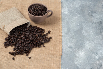 Bunch of medium roasted coffee beans out of sackcloth on marble surface