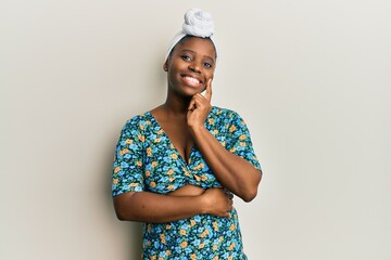 Young african woman wearing hair turban and african style looking confident at the camera with smile with crossed arms and hand raised on chin. thinking positive.