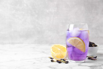 Glass of organic blue Anchan with lemon and ice on white marble table, space for text. Herbal tea