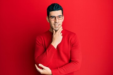 Obraz premium Handsome hispanic man wearing casual clothes and glasses smiling looking confident at the camera with crossed arms and hand on chin. thinking positive.