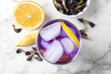 Glass of organic blue Anchan with lemon and ice on white marble table, flat lay. Herbal tea