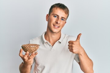 Young caucasian man holding lentils bowl smiling happy and positive, thumb up doing excellent and approval sign