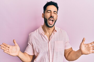 Fototapeta premium Young hispanic man wearing casual clothes celebrating mad and crazy for success with arms raised and closed eyes screaming excited. winner concept