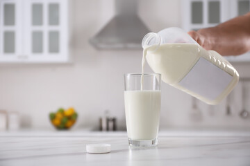 Man pouring milk from gallon bottle into glass at white marble table in kitchen, closeup. space for text