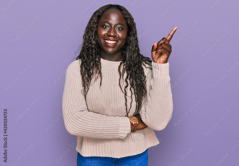 Sticker young african woman wearing wool winter sweater with a big smile on face, pointing with hand finger 