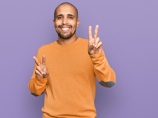 Hispanic adult man wearing casual winter sweater smiling looking to the camera showing fingers doing victory sign. number two.