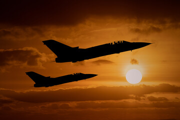 Fighter jets silhouettes at sunset, interceptor military aircraft on a combat mission to intercept...