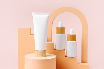 Cream tube with white dropper bottles on beige stairs with  geometric shapes and podium. Background for branding and packaging presentation. Natural skincare beauty product concept.