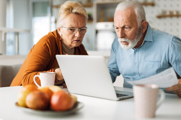 Shocked senior couple reading their home finances on laptop