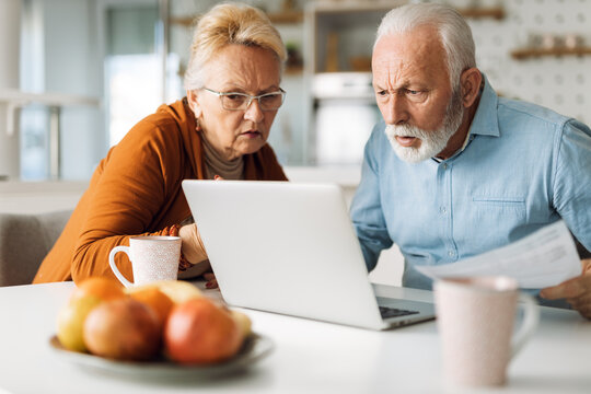 Shocked senior couple reading their home finances on laptop