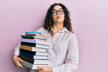 Young brunette woman with curly hair holding a pile of books looking at the camera blowing a kiss being lovely and sexy. love expression.