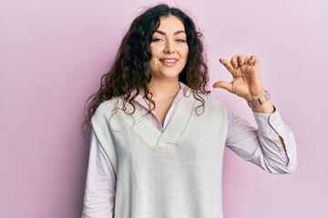 Young brunette woman with curly hair wearing casual clothes smiling and confident gesturing with hand doing small size sign with fingers looking and the camera. measure concept.