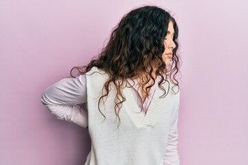 Fototapeta premium Young brunette woman with curly hair wearing casual clothes suffering of backache, touching back with hand, muscular pain
