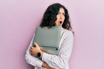 Fototapeta premium Young brunette woman with curly hair hugging laptop with love angry and mad screaming frustrated and furious, shouting with anger. rage and aggressive concept.