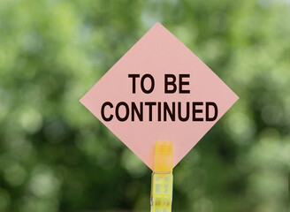 TO BE CONTINUED - text on pink note paper on green background.