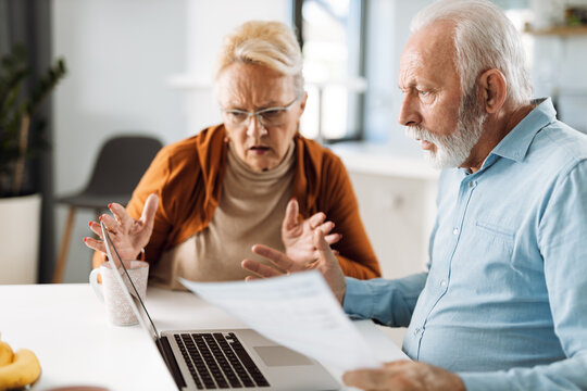 Shocked senior couple reading their financial bills at home