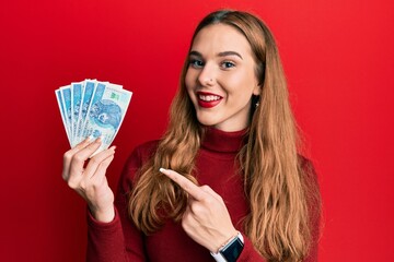 Young blonde woman holding 50 polish zloty banknotes smiling happy pointing with hand and finger