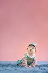 Asian happy cute baby smiling, sitting on carpet. 6 months baby on pink copy space as concept of bedroom, development, health, mood and motion of baby and kid department in hospital