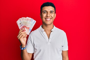 Young arab man holding colombian pesos looking positive and happy standing and smiling with a...